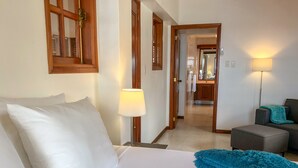 Habitación de hotel con cama, mesita de noche, lámpara, sofá y vista a la cocina.