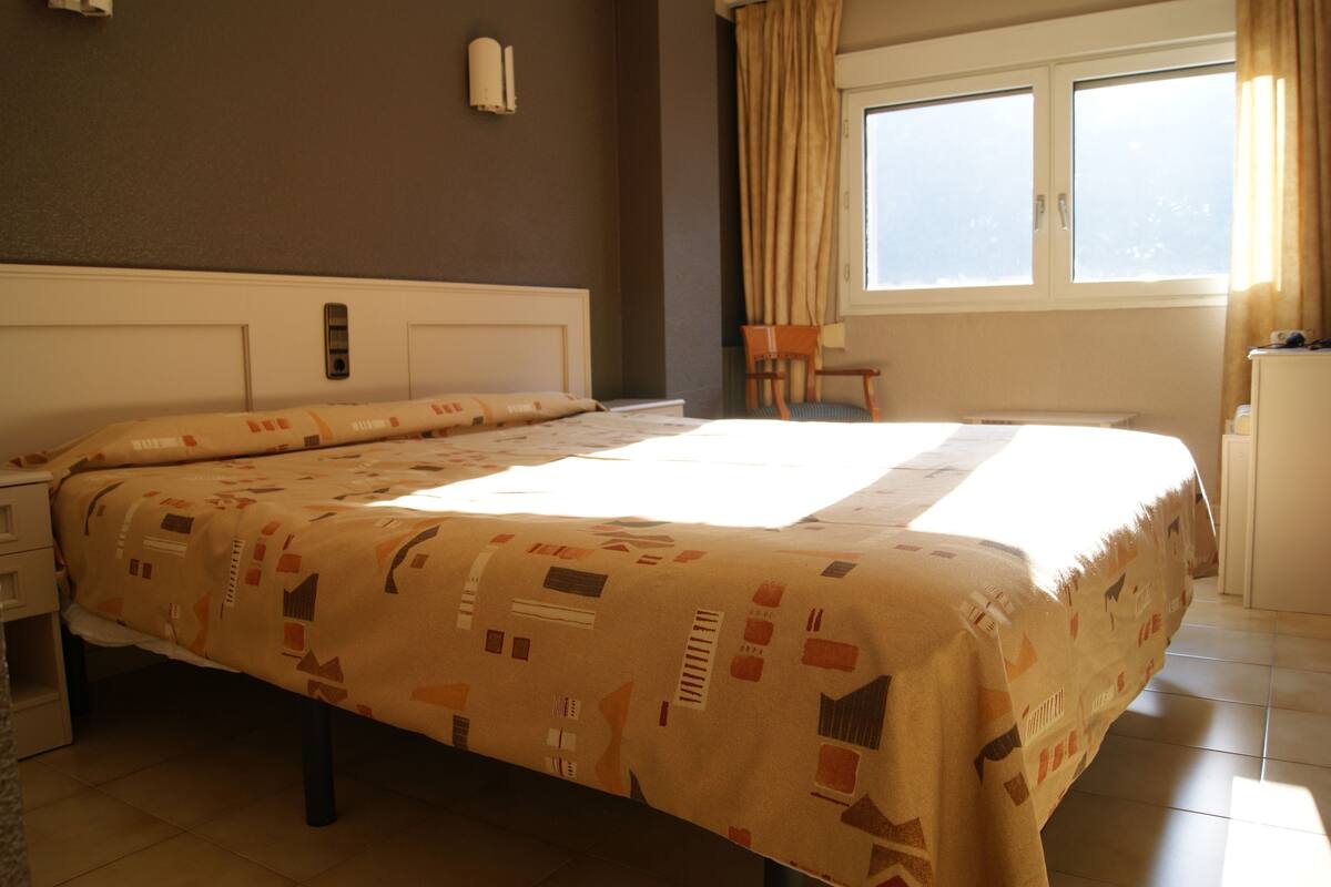 A hotel room with a bed, a chair, a desk, and a window with curtains.