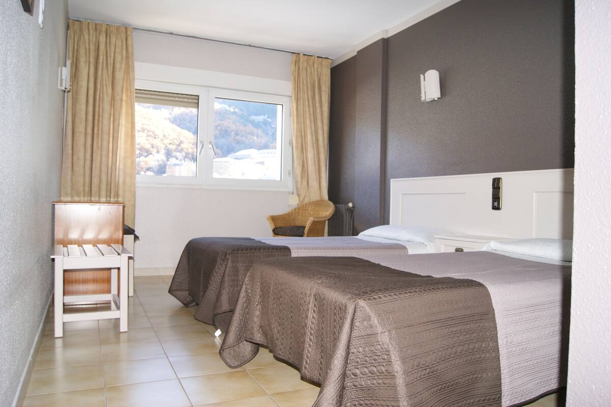 A hotel room with two beds, a chair, and a window with curtains.