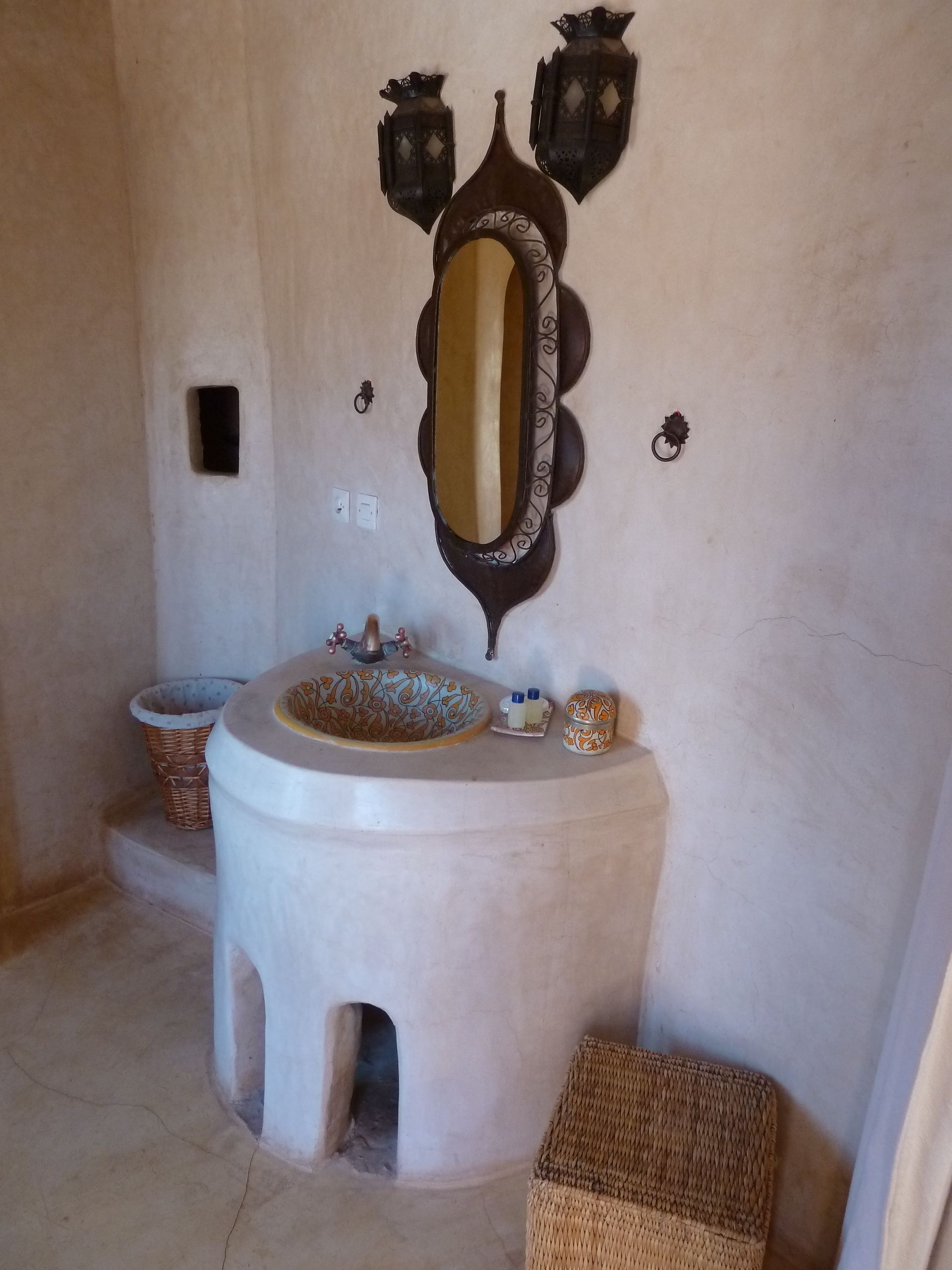 A bathroom with a round sink, a mirror with ornate frame, and two wall-mounted lanterns.