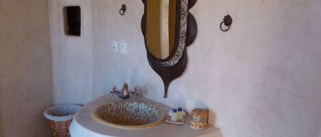 A bathroom with a round sink, a mirror with ornate frame, and two wall-mounted lanterns.