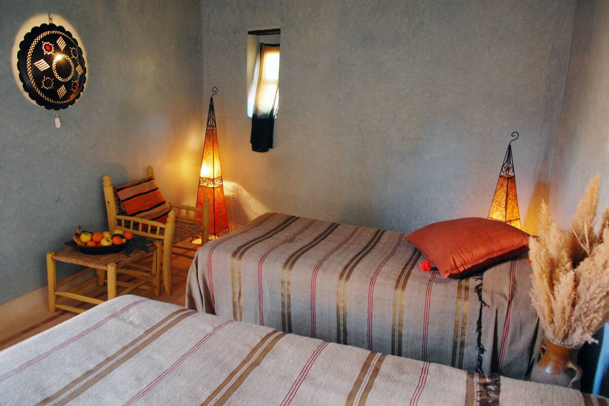 A cozy room with two beds, a chair, a small table with fruit, and decorative wall lights.