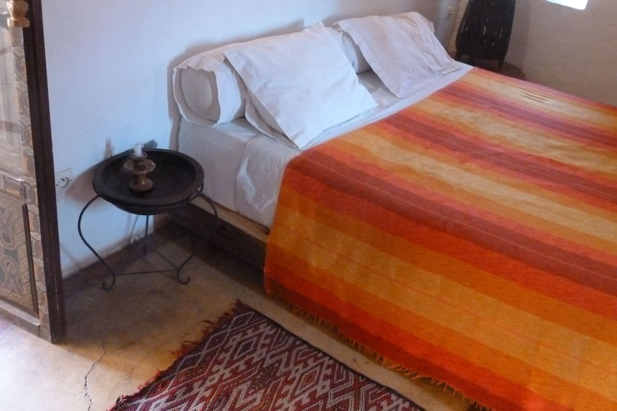 A bed with a striped blanket, a small table with a candle, and a patterned rug.