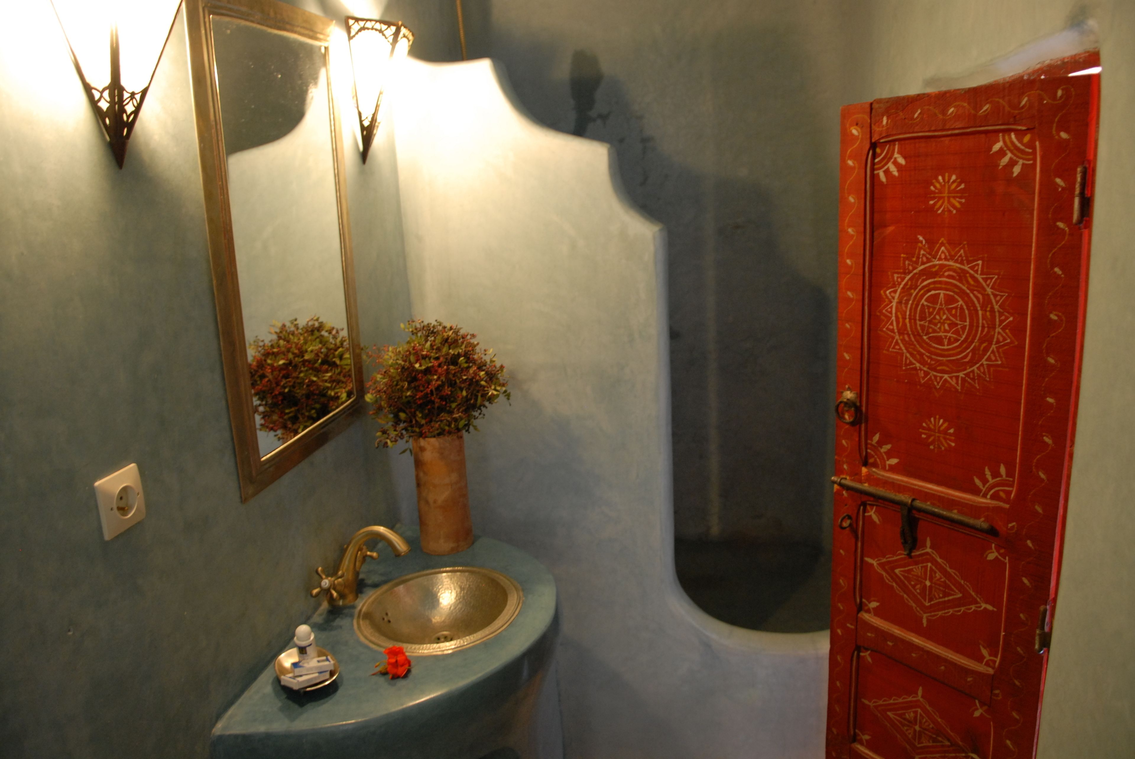 A bathroom with a blue sink, a mirror, and a red door with decorative patterns.