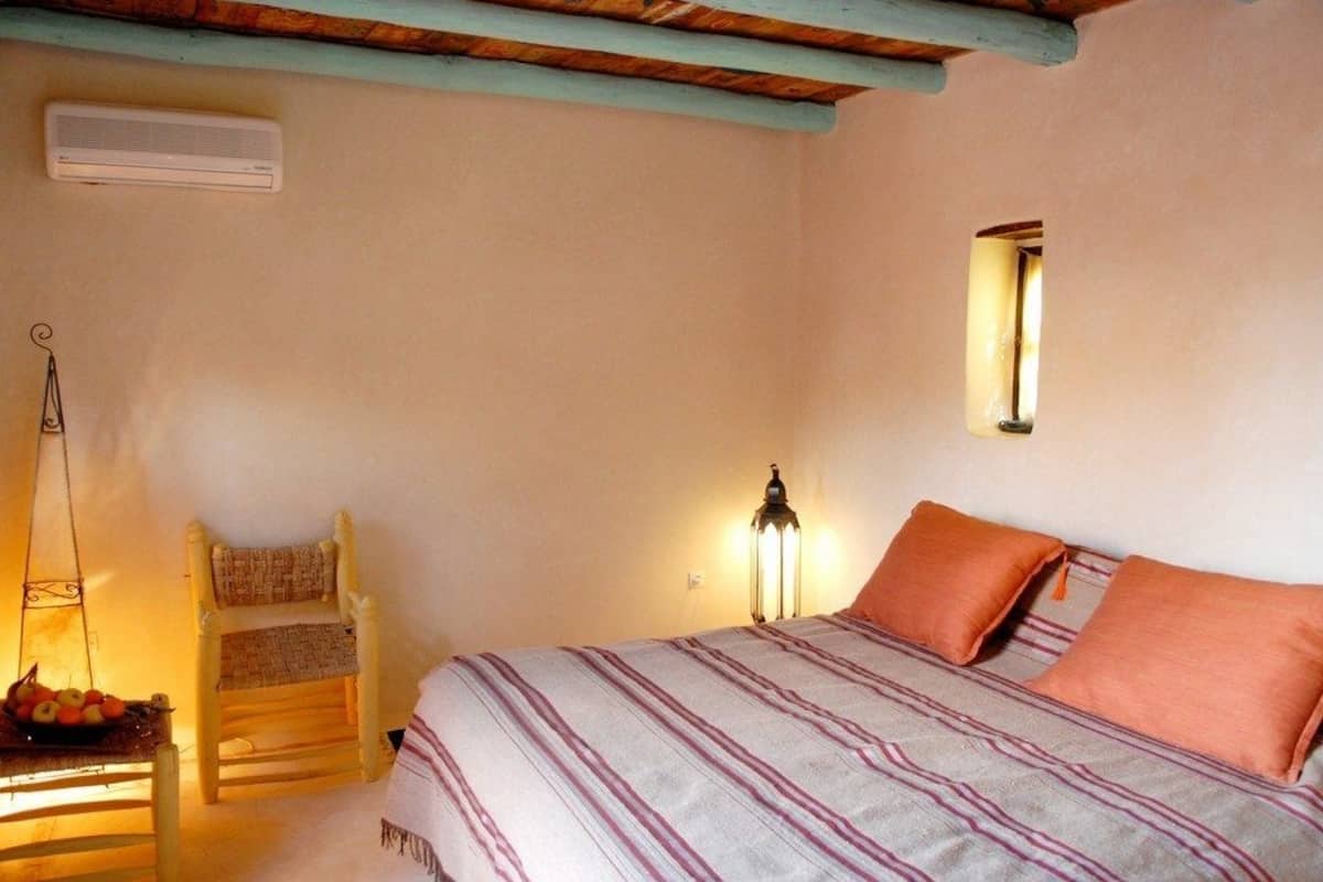 A bedroom with a bed, a chair, a lamp, and a small window.