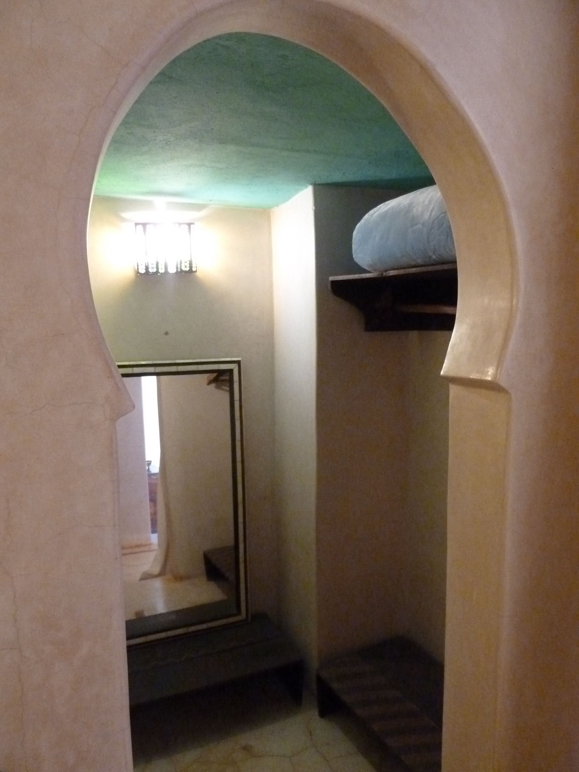 A narrow hallway with a mirrored closet door, a small bench, and a shelf with a mattress.