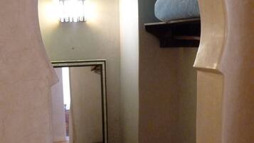 A narrow hallway with a mirrored closet door, a small bench, and a shelf with a mattress.
