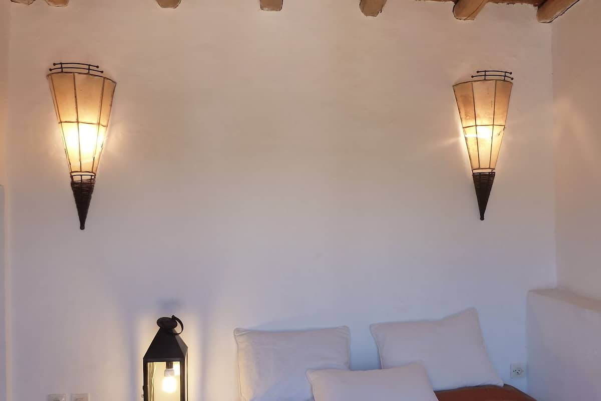 A bedroom with a wooden ceiling, two wall-mounted lights, a bedside table with a lantern, and a bed with striped bedding.