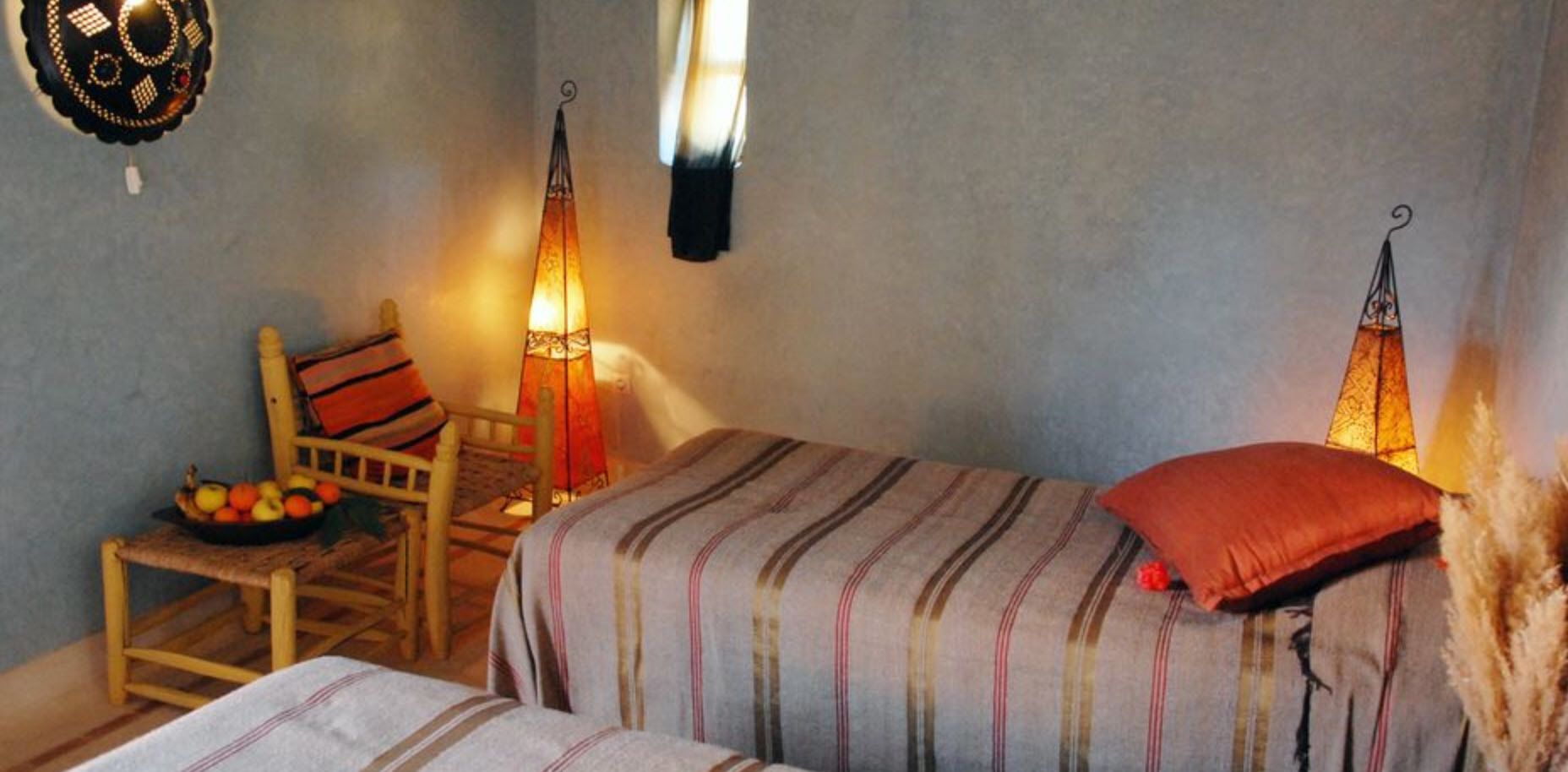 Una habitación acogedora con dos camas, una silla de madera, un frutero y luces decorativas en la pared.