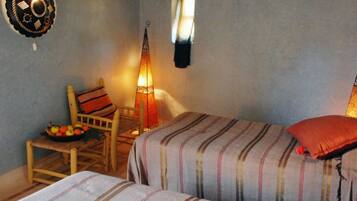 Una habitación acogedora con dos camas, una silla de madera, un frutero y luces decorativas en la pared.