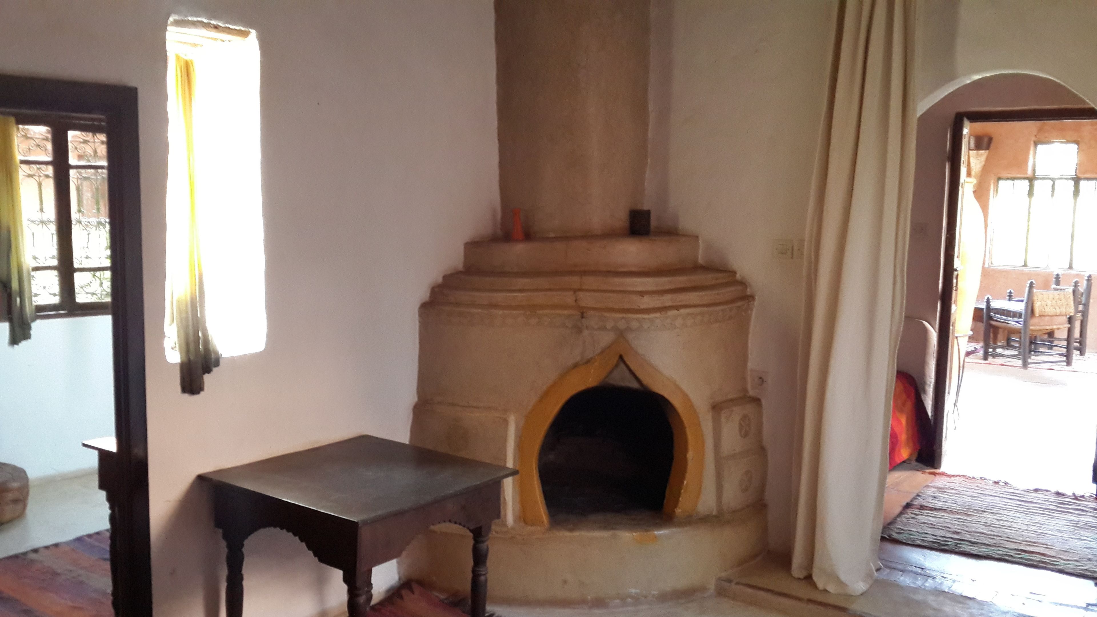 A room with a stone fireplace, a small table, and a window with curtains.