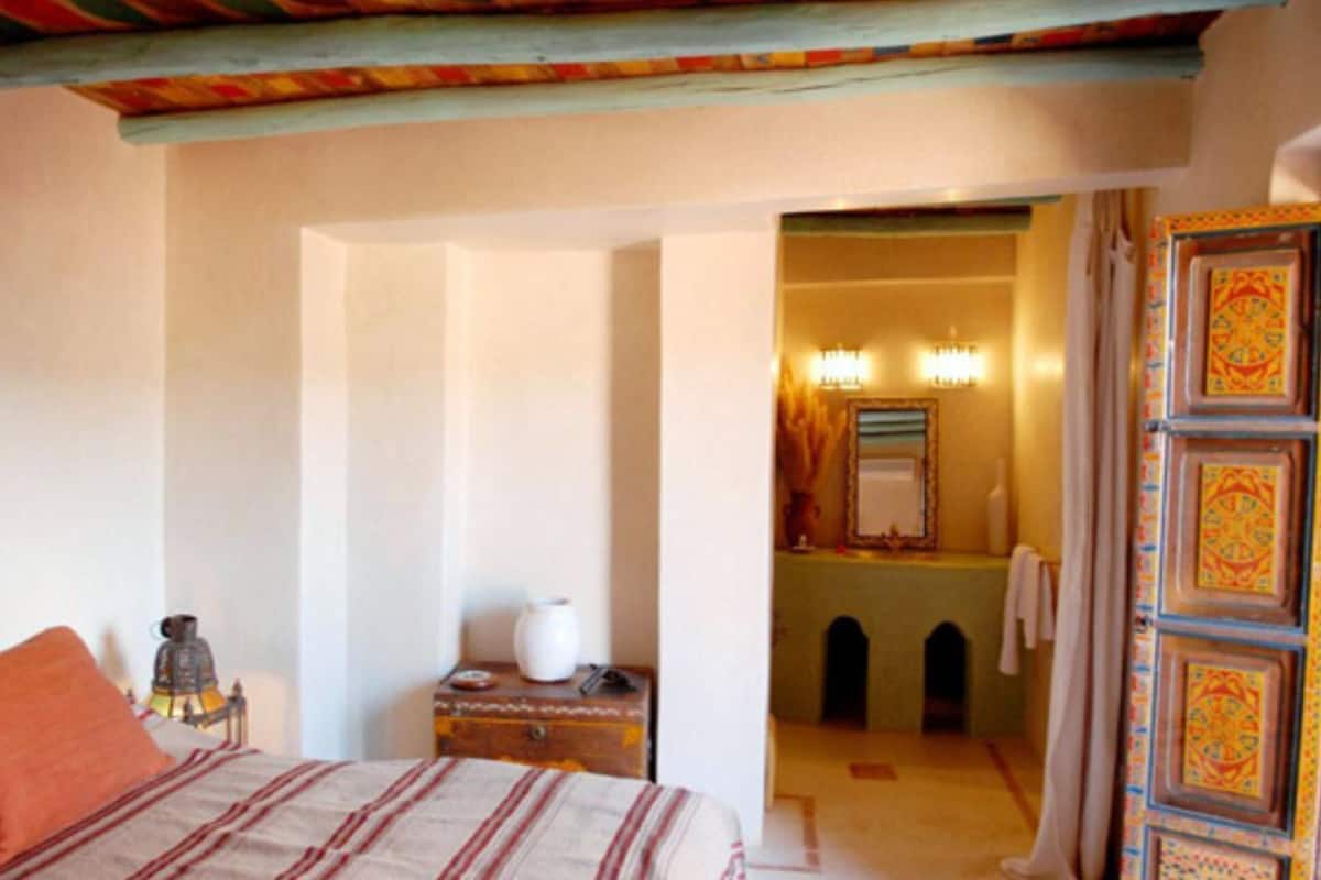 A bedroom with a bed, a nightstand, a vase, and a door leading to a bathroom.