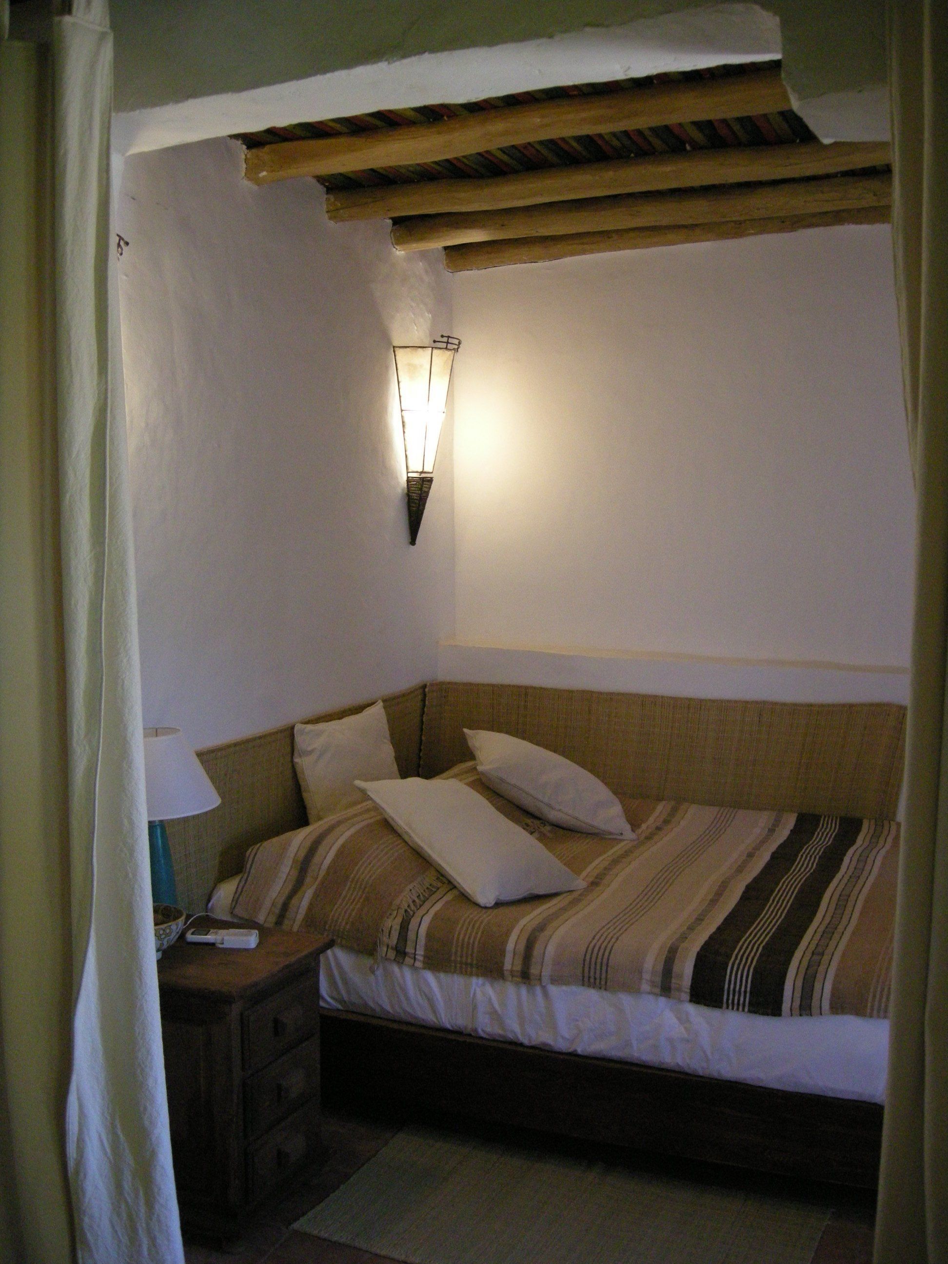 A bedroom with a single bed, a nightstand, a lamp, and a wall-mounted light fixture.