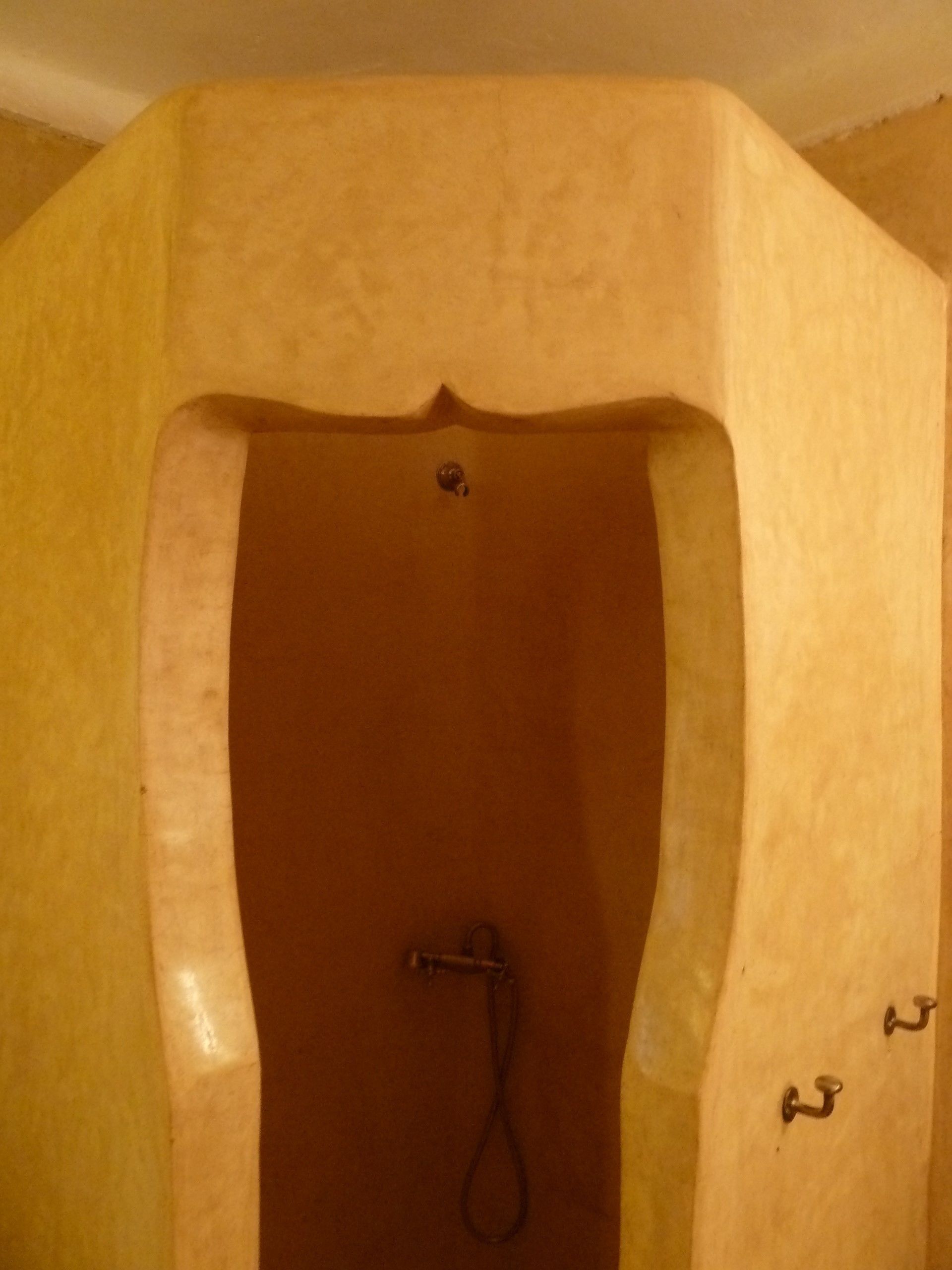 Une baignoire équipée d’un pommeau de douche et de deux crochets fixés au mur.