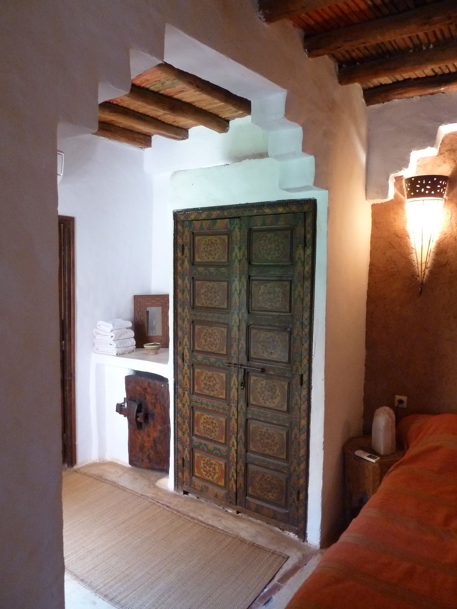 Une chambre traditionnelle avec une porte en bois, une petite étagère avec des serviettes et un luminaire fixé au mur.