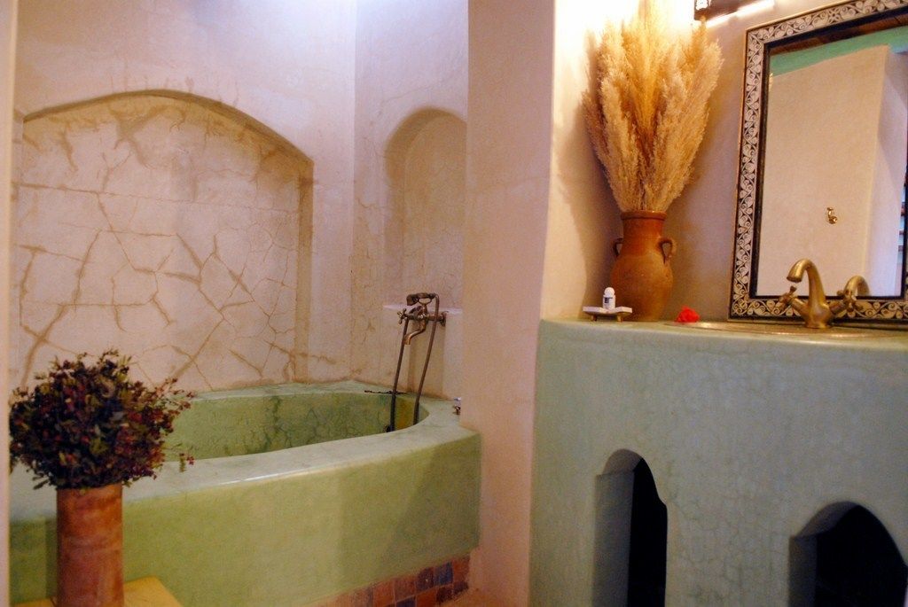 A bathroom with a green bathtub, a vase with dried flowers, and a mirror with a decorative frame.