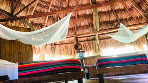 Una cabaña con techo de paja que tiene dos camas, cada una con ropa de cama de colores, y un dosel colgante.