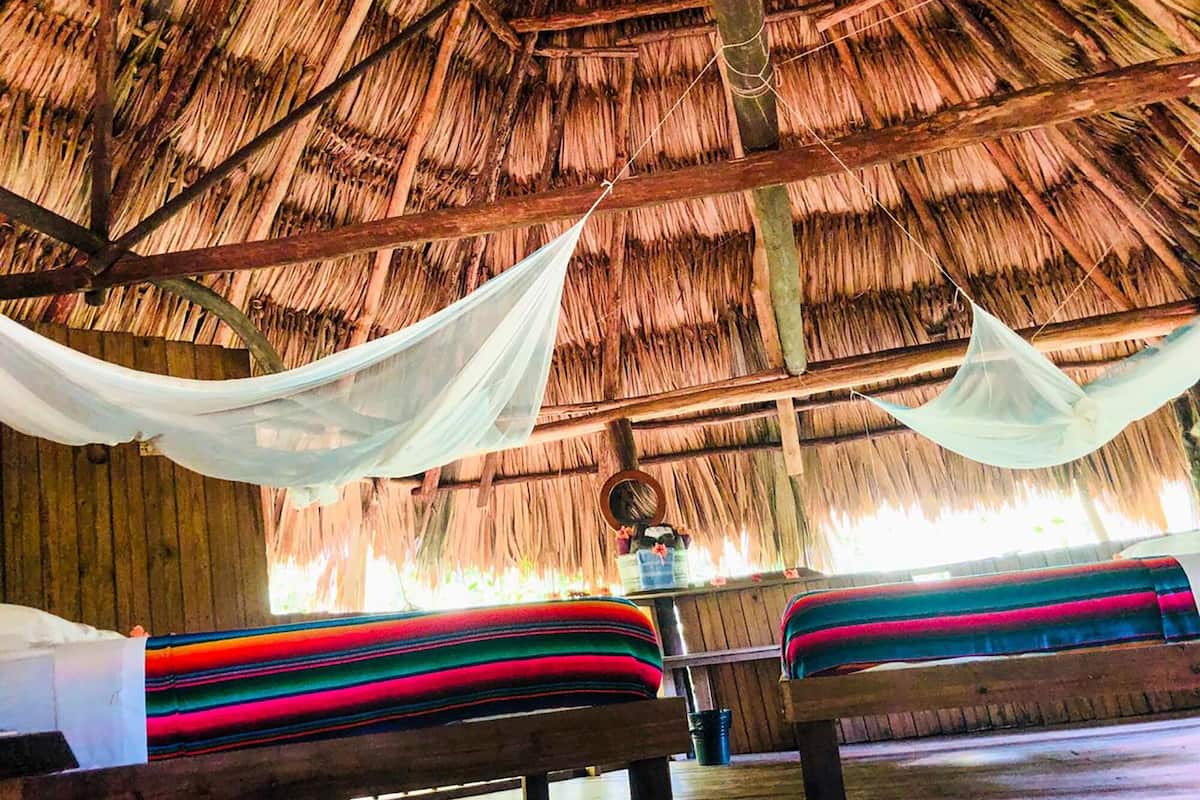 A thatched-roof hut with two beds, each with colorful bedding, and a hanging canopy.