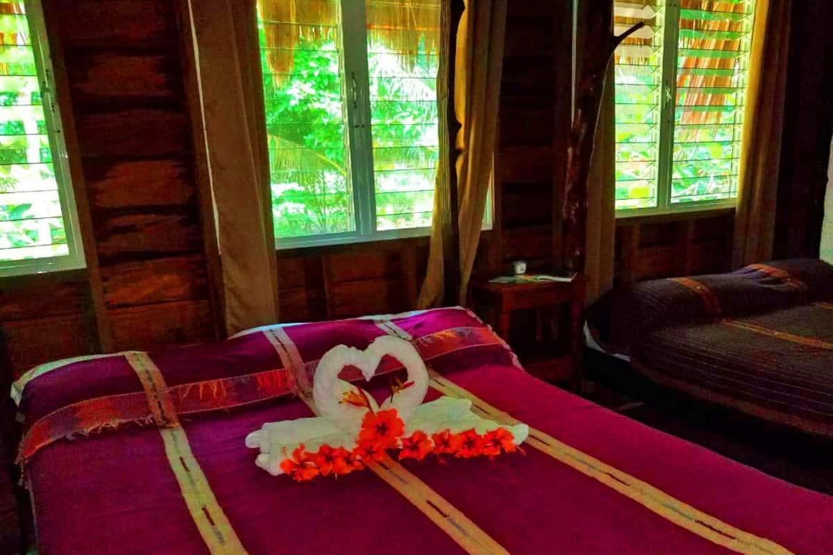 A bed with a heart-shaped decoration made of flowers and a swan, a wooden headboard, and a window with a view of greenery.