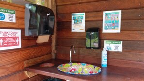 Un baño con lavamanos, dispensador de gel antibacterial y señalización sobre medidas de seguridad por COVID-19.