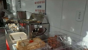 Een buffetgedeelte met diverse etenswaren en bakken, waaronder taart en macarons, met een bord waarop de openingstijden staan.