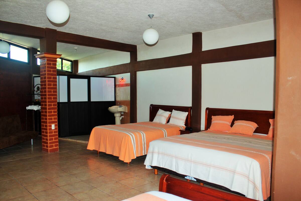 Habitación de hotel con dos camas, un pilar de ladrillo, un lavabo y una ventana.