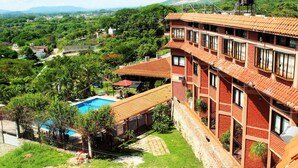 A multi-story building with a red-tiled roof, a swimming pool, and a view of a lush green landscape. - River Side Hotel (Chiapa de Corzo)