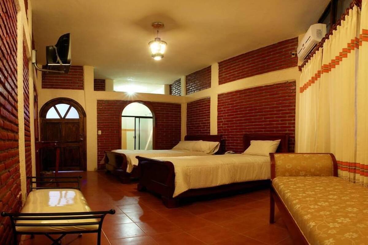 Una habitación de hotel con pared de ladrillo, una cama, un sofá, un escritorio y una ventana.