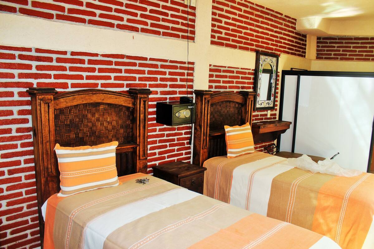 Habitación de hotel con dos camas, una pared de ladrillo, cabecero de madera y una mesita de noche con una radio.