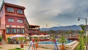 A hotel with a swimming pool, a children's play area, and a view of mountains. - River Side Hotel (Chiapa de Corzo)