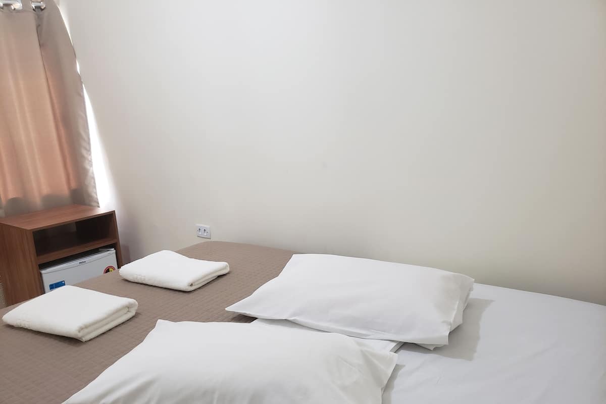 Une chambre d’hôtel avec un lit, des oreillers, une table de chevet en bois et un petit réfrigérateur.