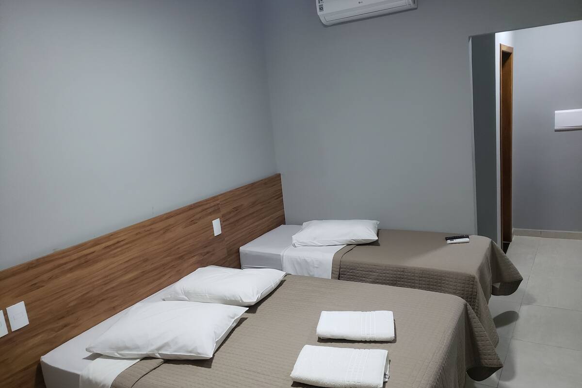 Une chambre d’hôtel avec deux lits, chacun doté d’une tête de lit en bois, de draps blancs et d’une télécommande sur le lit de droite.