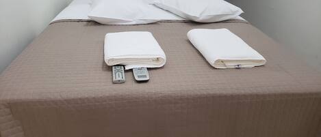 Un lit bien fait, avec des oreillers blancs et des serviettes pliées, une télécommande et un téléphone intelligent posés sur le lit.