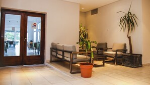 A spacious lobby with a sofa, chairs, a potted plant, and a wooden door leading to a dining area. - Hotel Ciudad del Sol (Termas de Rio Hondo)