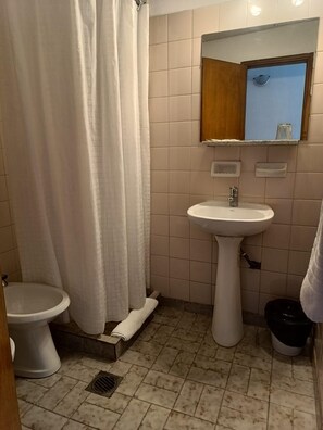A small bathroom with a toilet, a sink, and a shower curtain. - Hotel Iberia (Neuquén)