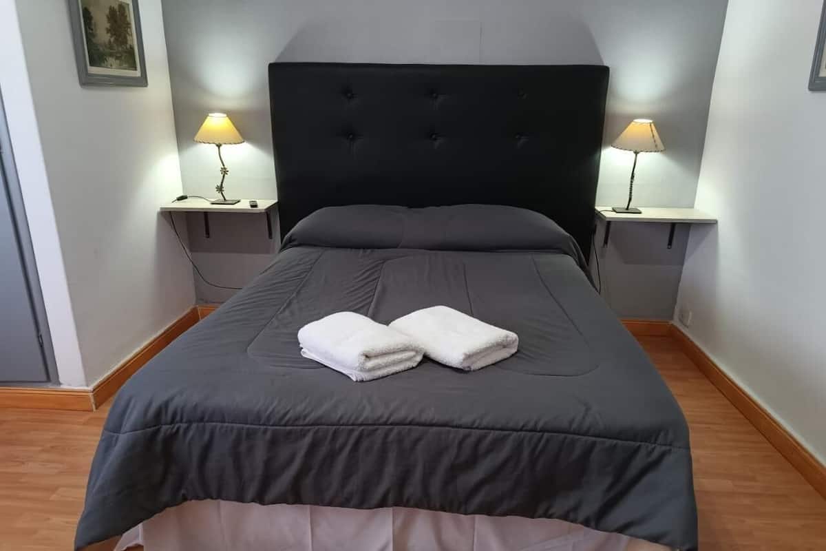 A neatly made bed with a dark headboard, two bedside lamps, and a pair of folded towels on the bed.