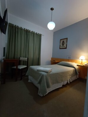A hotel room with a bed, a desk, a chair, a lamp, and a picture on the wall. - Hotel Iberia (Neuquén)