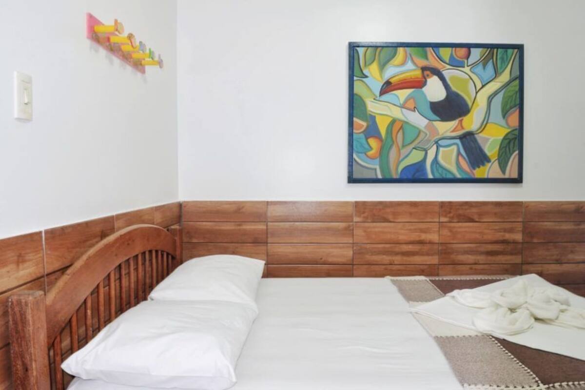 A room with a wooden headboard, a bed with white bedding, and a colorful abstract painting on the wall.