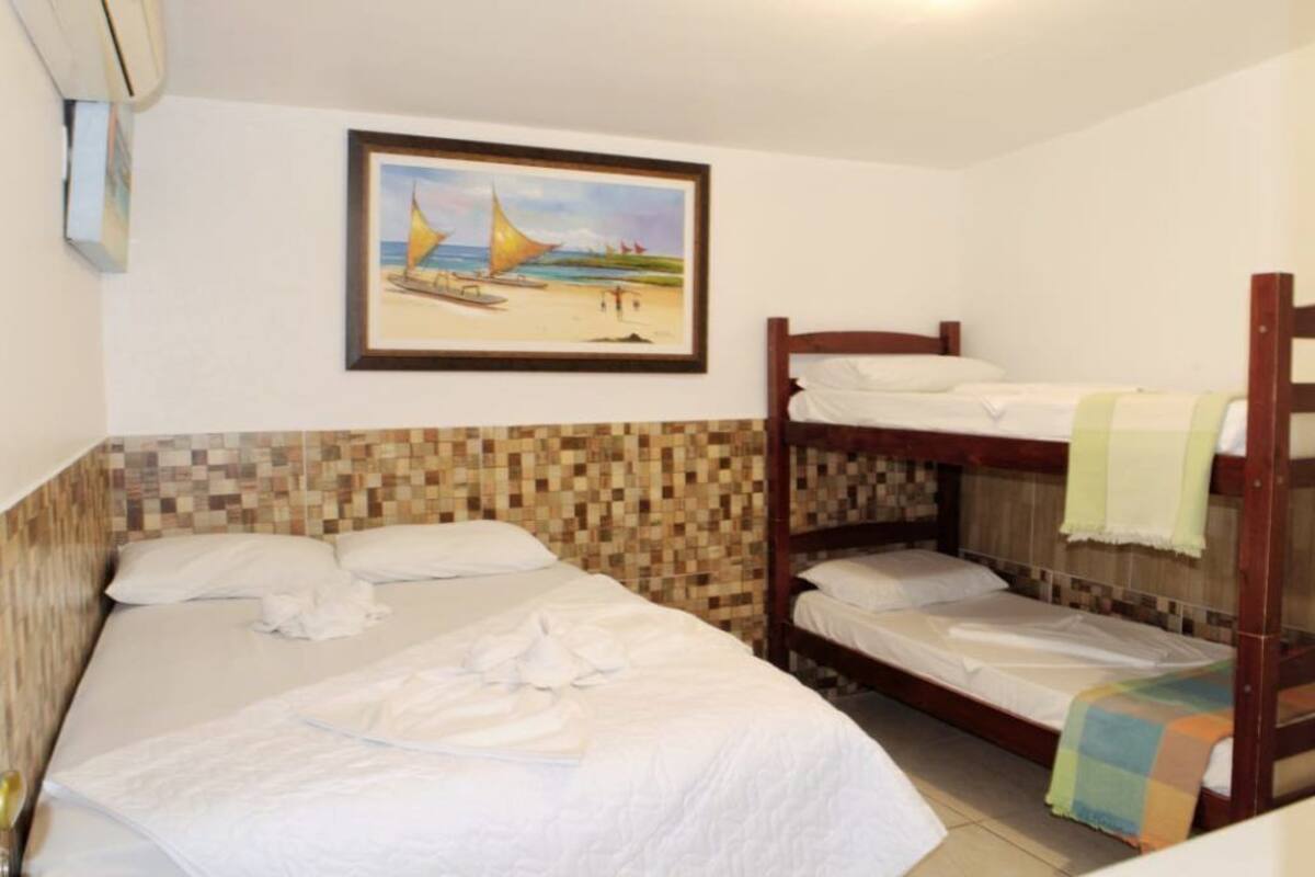 A room with two beds, one with a wooden headboard and the other with a metal frame. There is a painting of a beach scene on the wall above the beds.