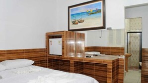 Habitación de hotel con cama, escritorio de madera, refrigerador y un cuadro de una playa.