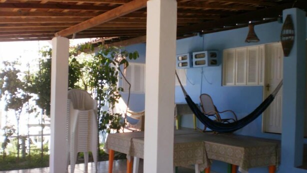 Un espacio al aire libre techado con una hamaca, una mesa con mantel y una silla.