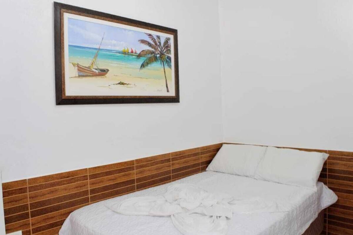 A single bed with a wooden headboard and a framed painting of a beach scene above it.
