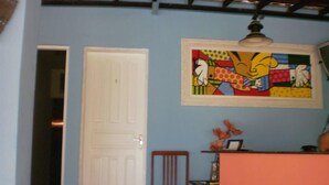 Una habitación con pared azul, puerta blanca, una silla de madera y un cuadro abstracto de colores.