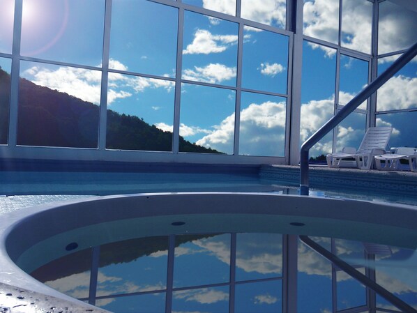 Piscina com água azul cristalina, rodeada por amplas janelas que oferecem vista para uma montanha e o céu.