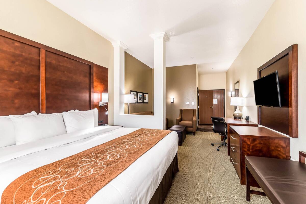 Una habitación de hotel con una cama grande, un escritorio, una silla, un televisor y un espejo.