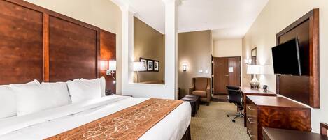 A hotel room with a large bed, a desk, a chair, a television, and a mirror.
