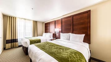 Ein Hotelzimmer mit zwei Betten, einem großen Holzkopfteil, einem Schreibtisch mit Lampe und einem Fenster mit Vorhängen.