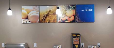 A food service area with a grill station, waffle makers, and a digital menu display.