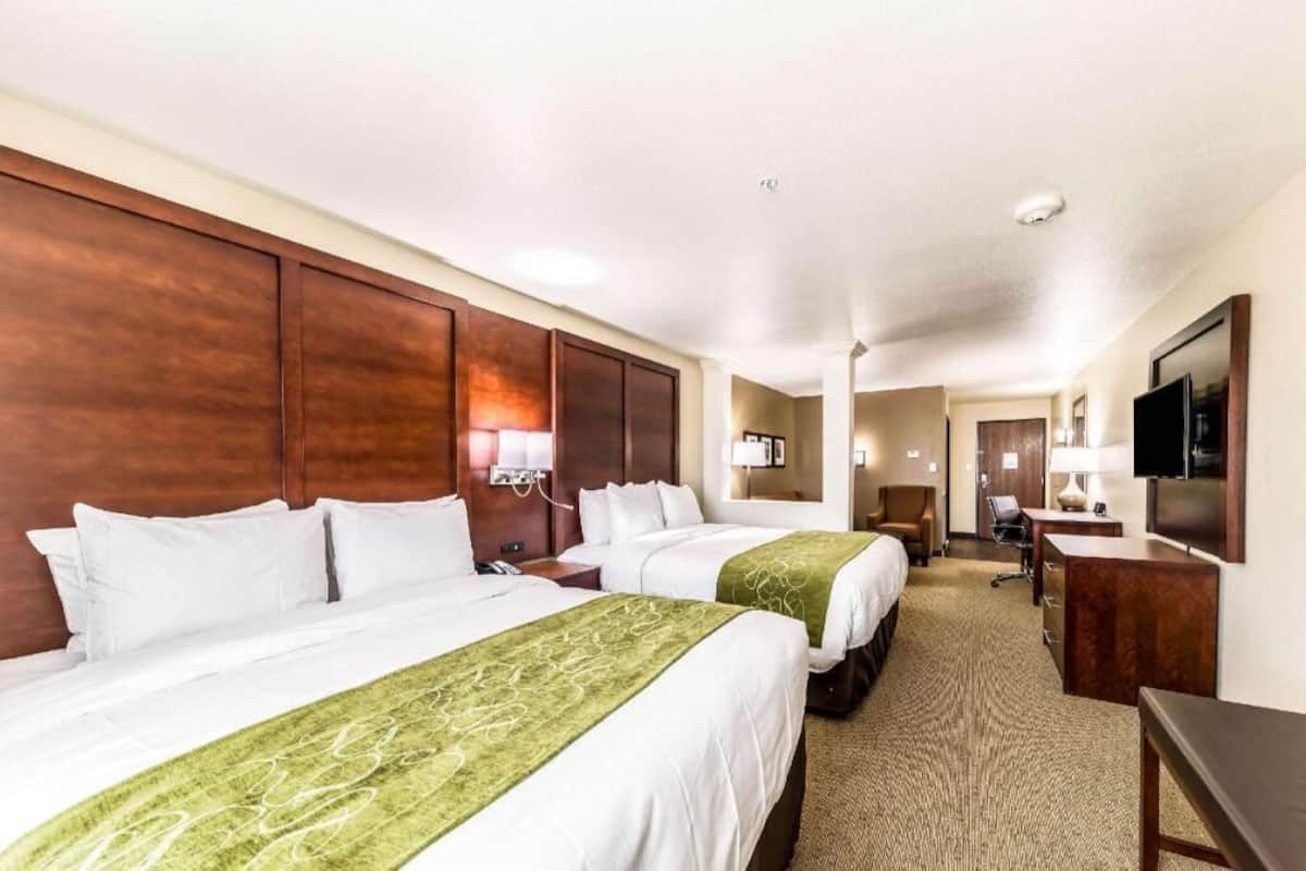 Habitación de hotel con dos camas, un escritorio, una silla, un televisor y un baño al fondo.