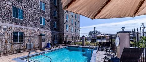 A swimming pool with a stone building in the background, outdoor seating, and a lifeguard stand.